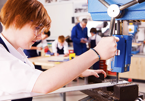 A pupil being taught skills in STEM by using a drilling tool in a technology lesson