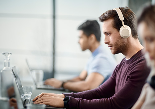 Gentleman wearing beige version of Jabra Evolve2 65 headset at desk