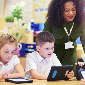 Teacher in classroom with children in uniform using tablet devices