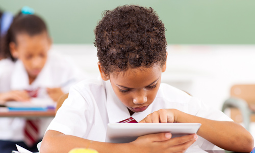 young boy in school uniform using 1:1 tablet device