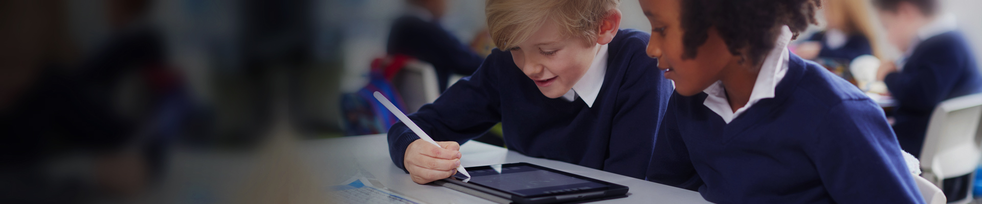 School pupils sat at a desk in a classroom using a device
